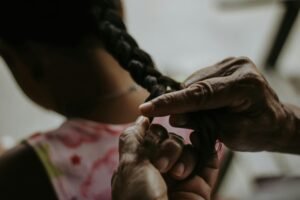 A close-up image capturing an adult braiding a child